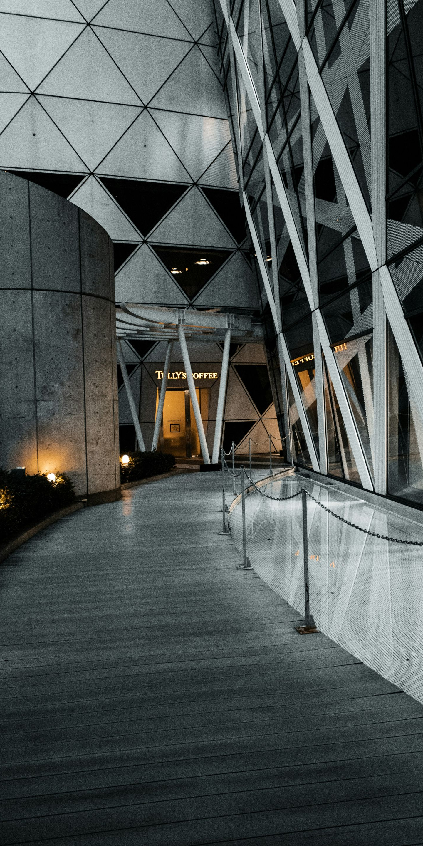 Curved walkway beside geometric building columns at night, lit by warm lights