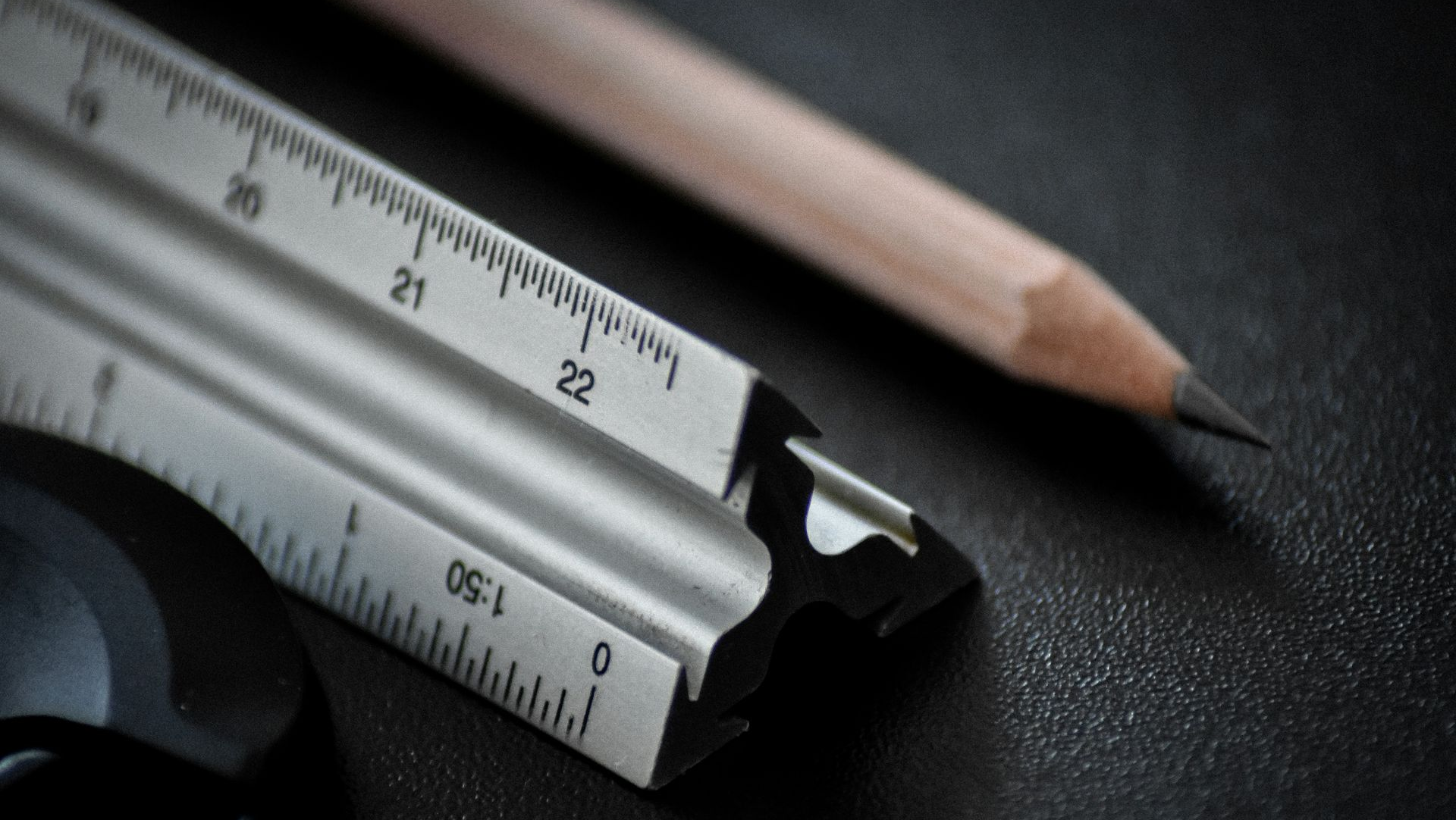 Close-up of a silver utility knife and pencil on a dark textured surface