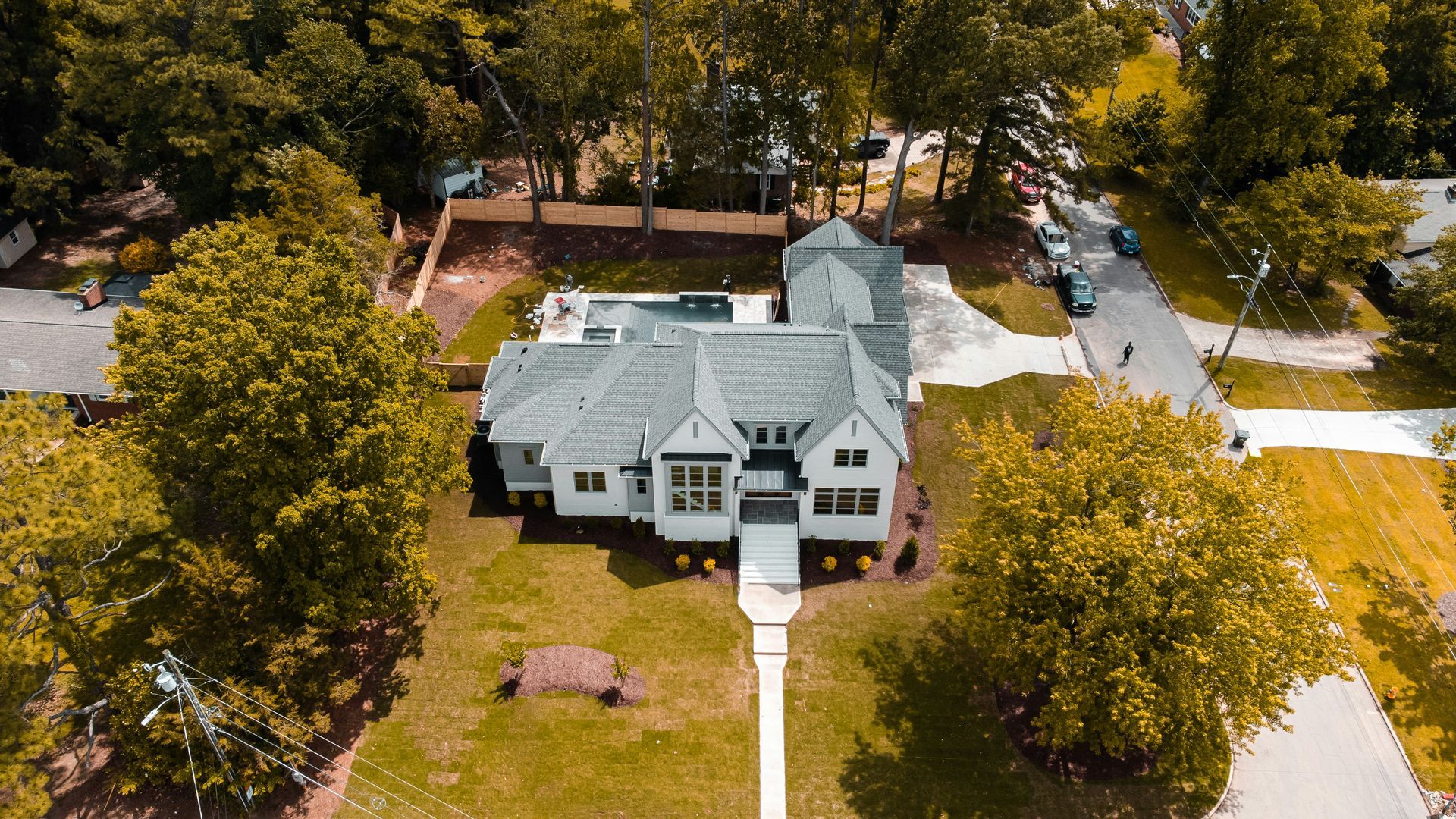 Aerial view of a large white house with a front yard, surrounded by trees and a driveway.