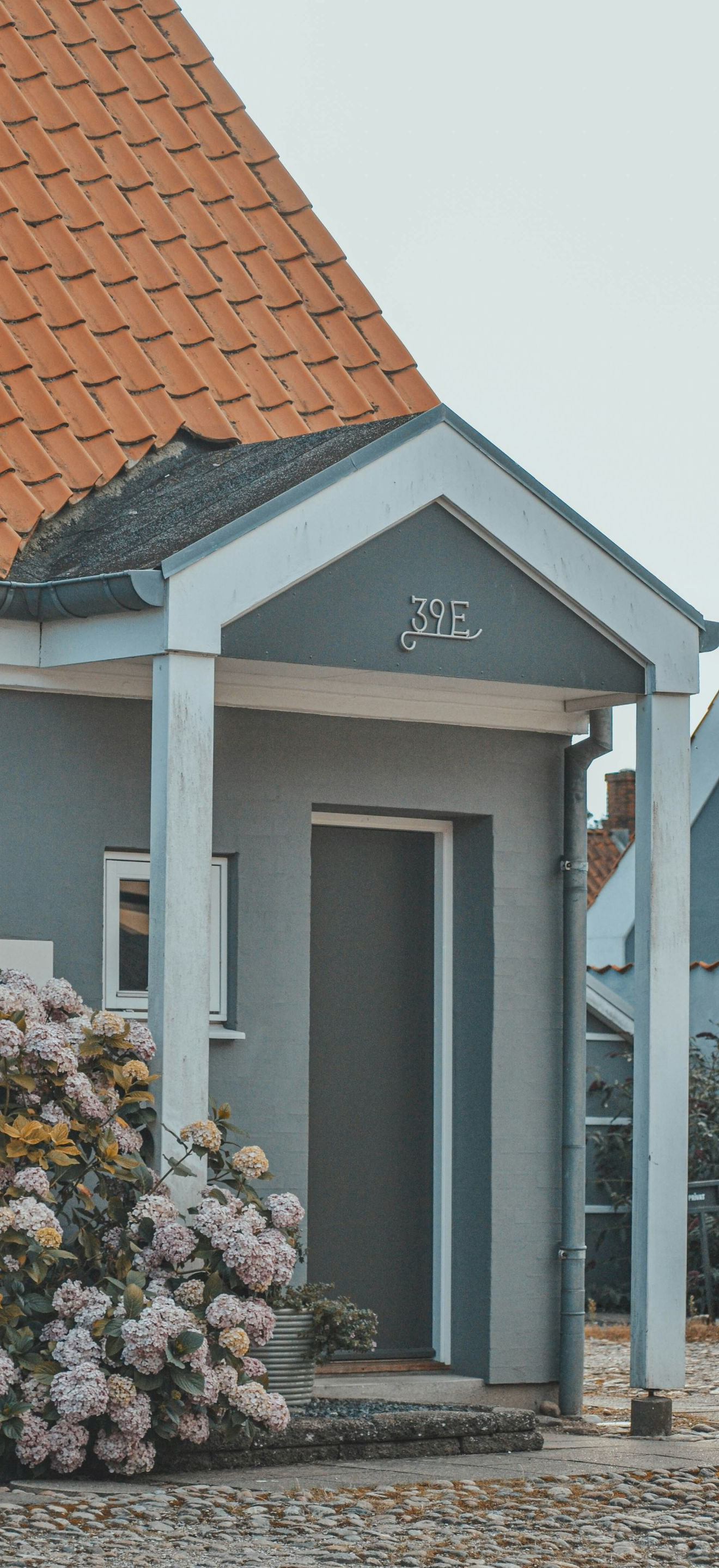 Small gray house entrance with a red-tiled roof and potted flowers by the door