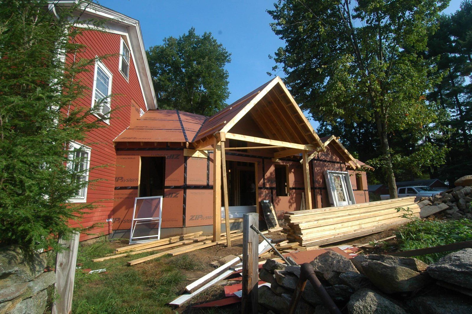 House under renovation with wooden framing, red siding, and construction materials in the yard