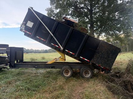 Black dump trailer tipped up on a field, with a tractor attached, unloading material.