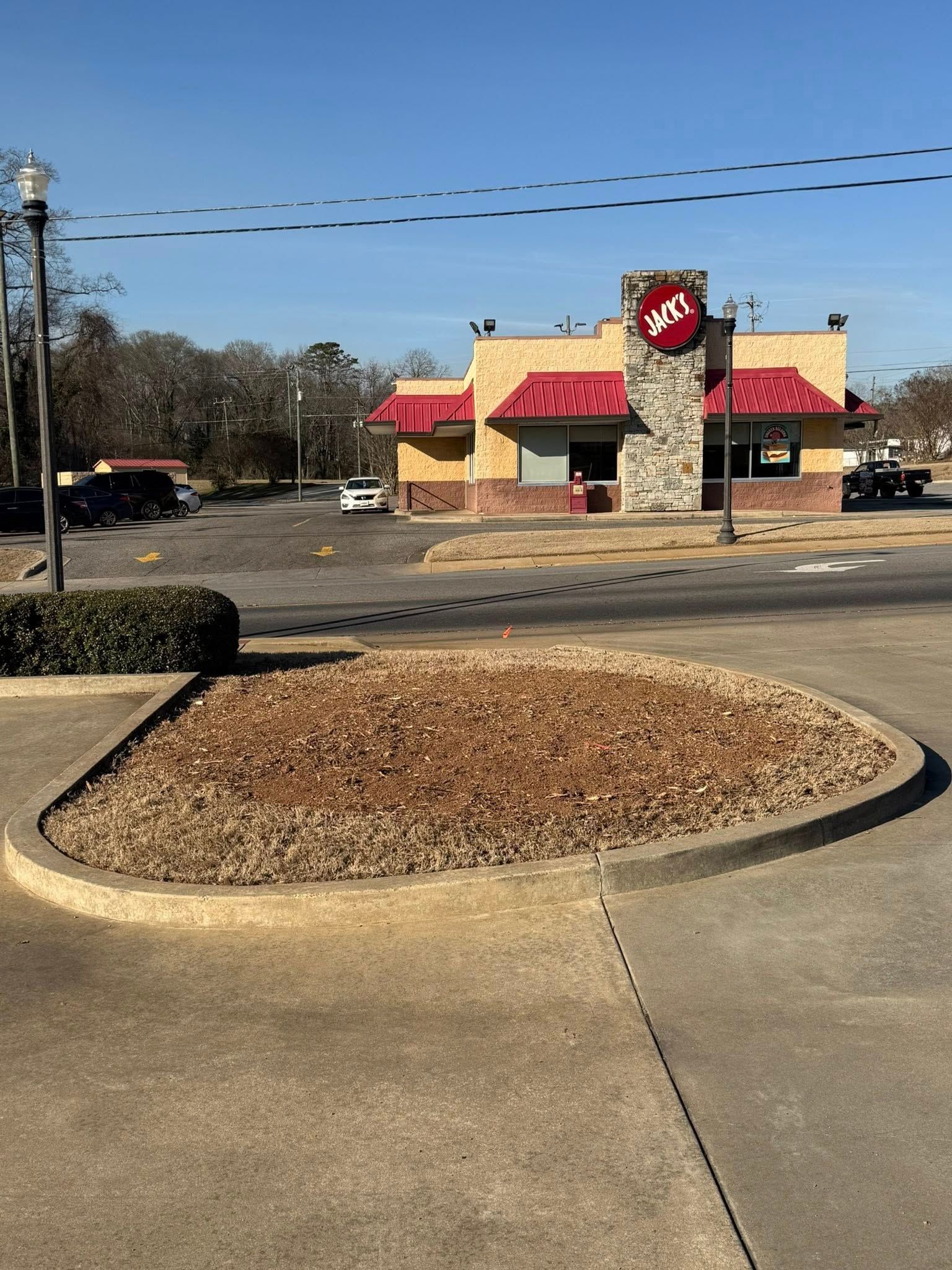 Fast-food restaurant with red roof and stone tower in a parking lot, seen across a landscaped curb island.