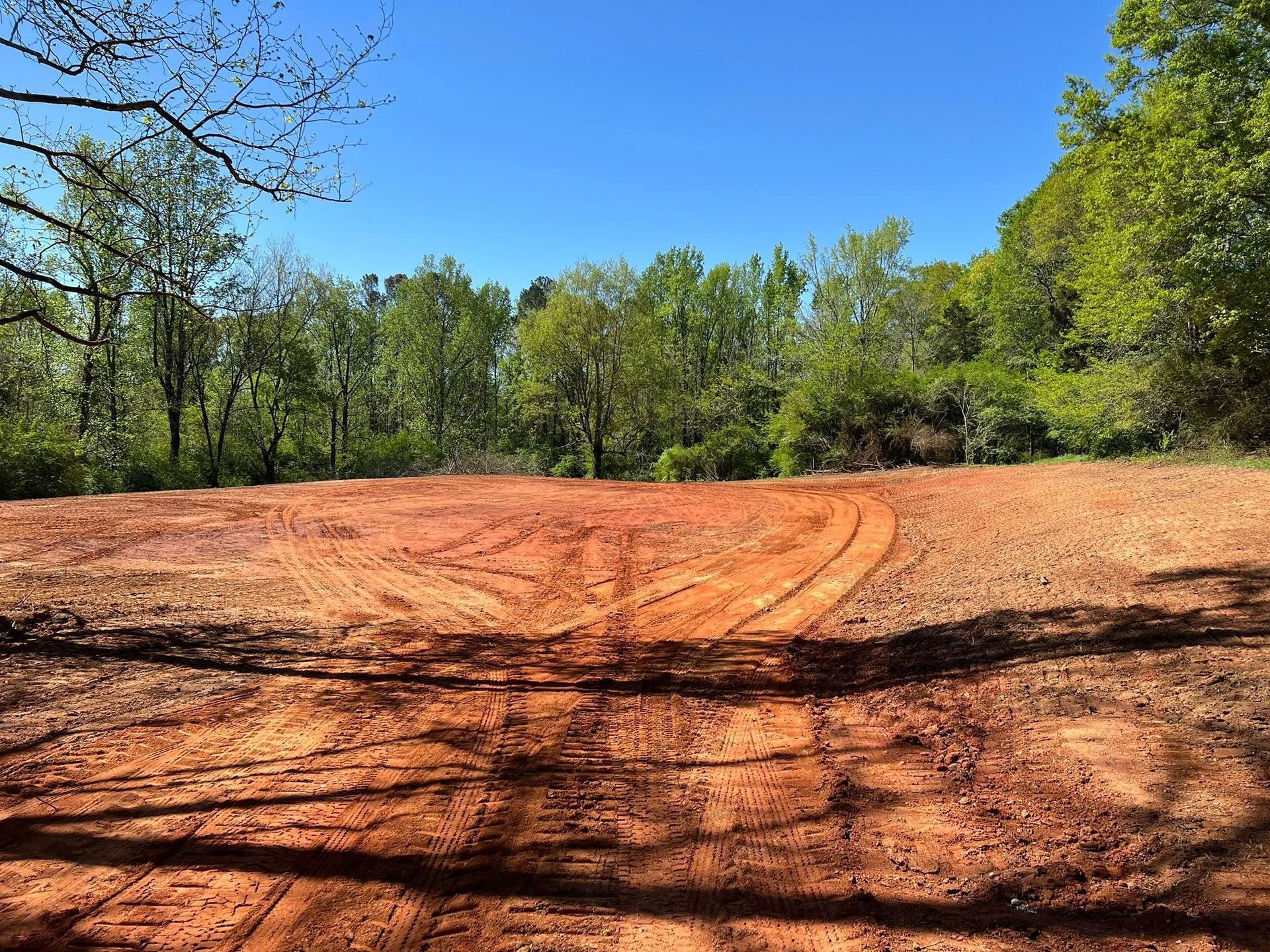 Red dirt road curving through a wooded clearing under a bright blue sky