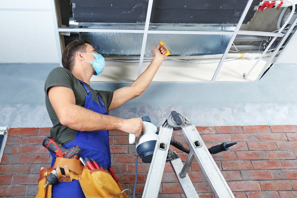 Male Technician Cleaning Industrial Air Conditioner Indoors, Ducted Air Conditioning Systems in Townsville