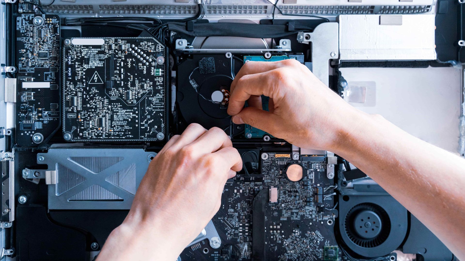 Hands installing a hard drive inside the open case of a computer.