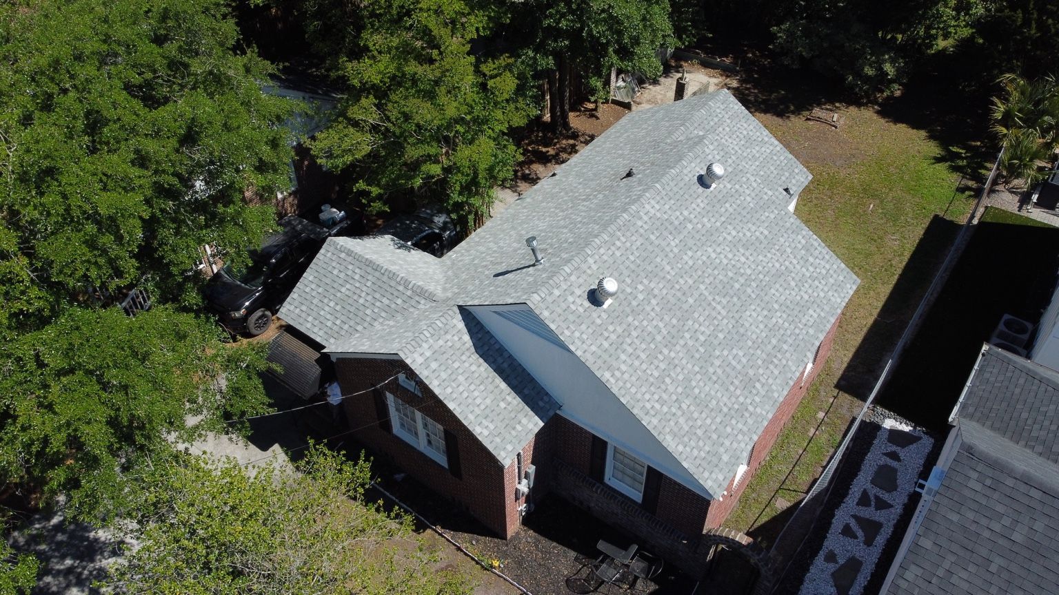 Finished light gray architectural shingle roof on a brick home surrounded by trees