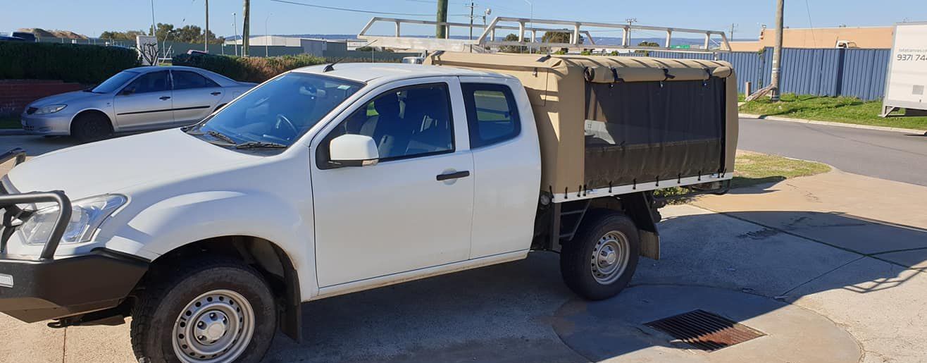White Isuzu D-Max utility vehicle with a custom-fitted canvas canopy over the tray and a metal roof rack installed