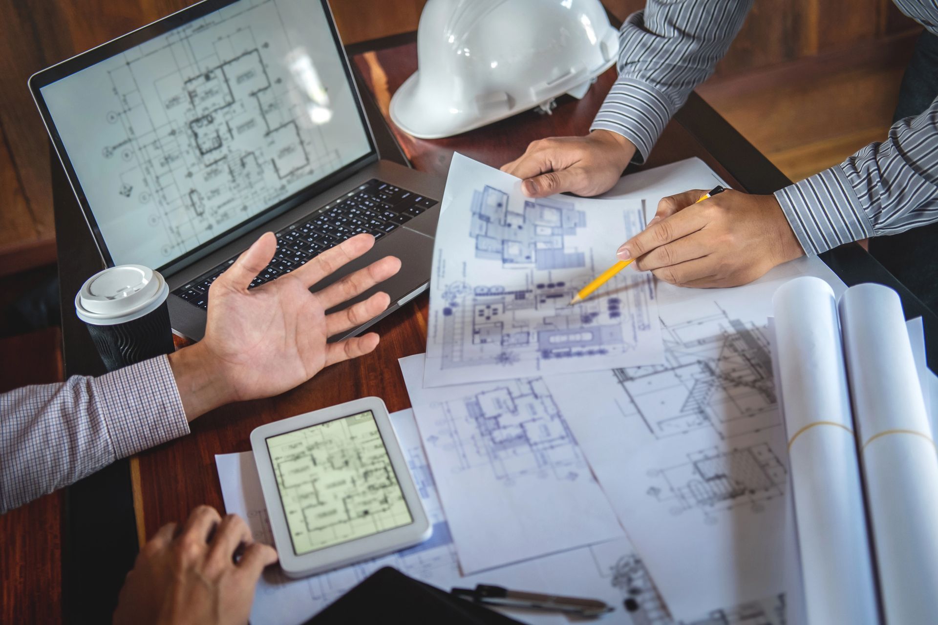 Dos personas revisando planos arquitectónicos, planos y una tableta, con una computadora portátil,