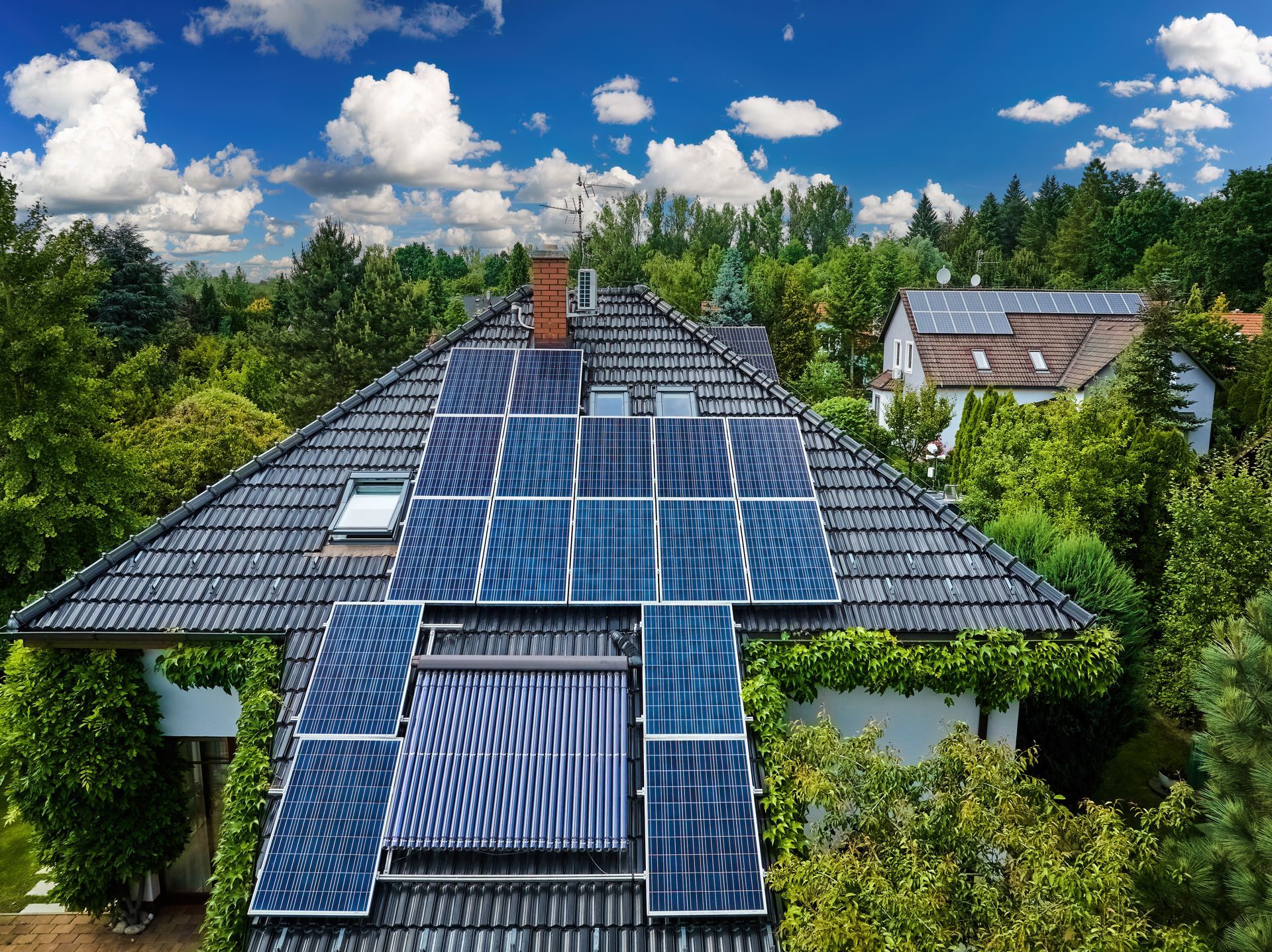 Paneles solares instalados en el techo de una casa rodeada de árboles verdes bajo un cielo azul con nubes.