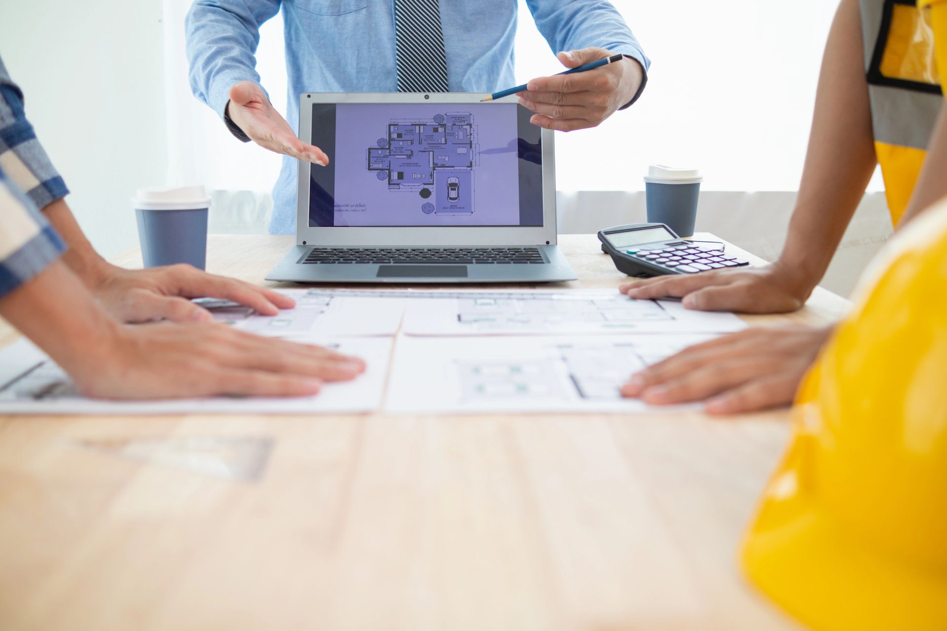 Personas revisando planos y una computadora portátil con un diseño, uno apuntando a la pantalla.
