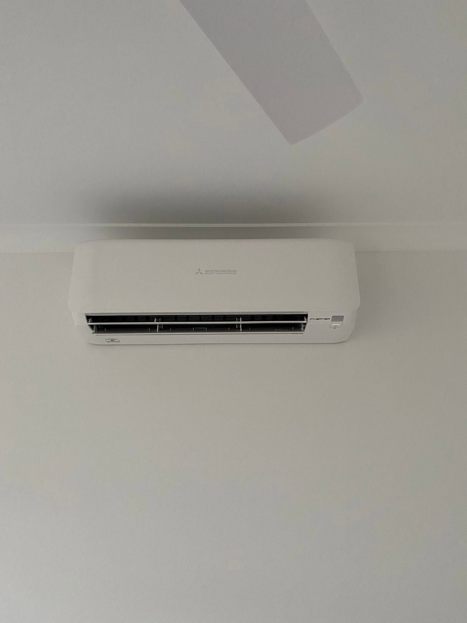 White wall-mounted air conditioner on a light-colored wall near a ceiling fan.