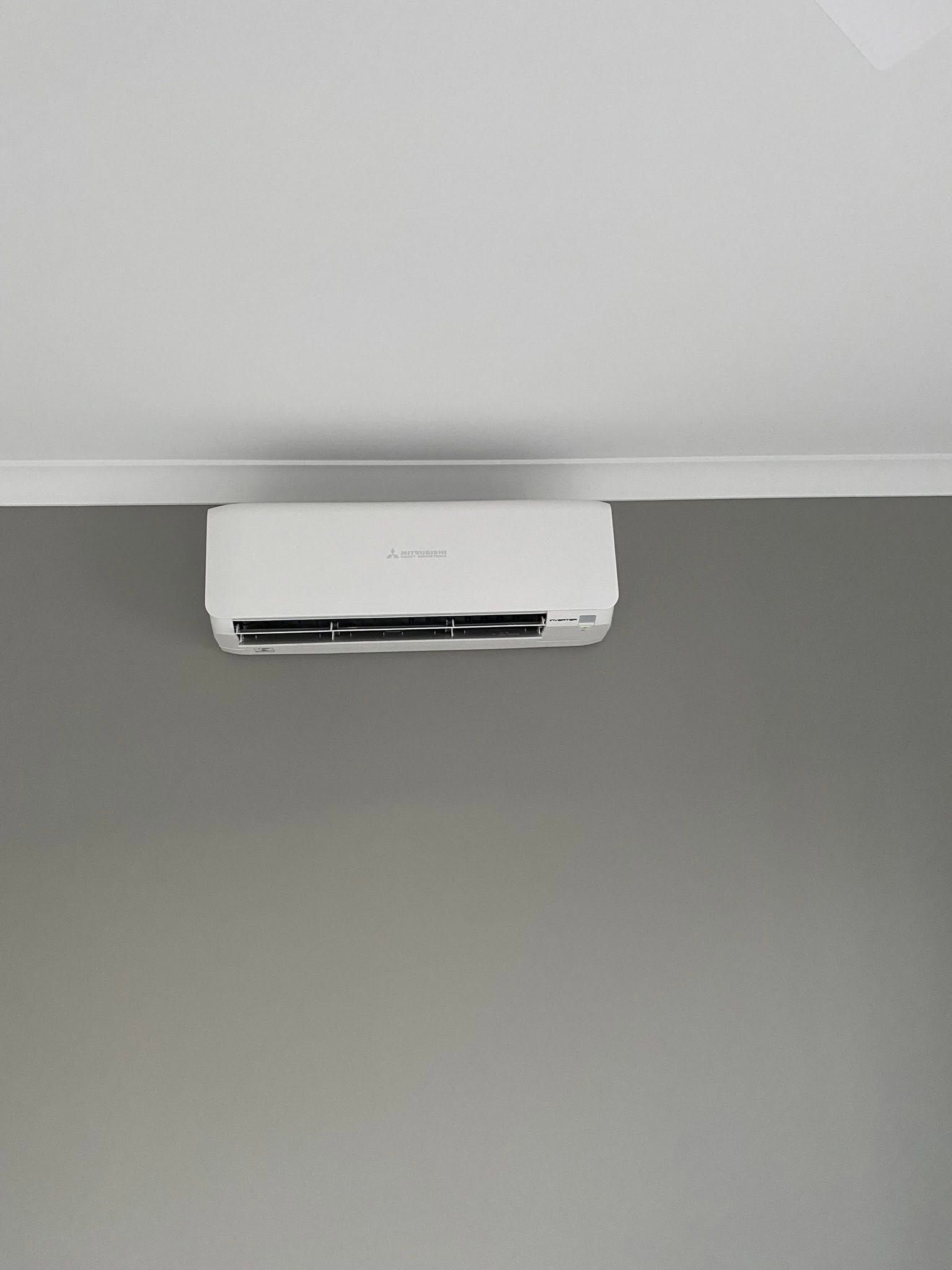 White wall-mounted air conditioner near the ceiling above a gray wall.