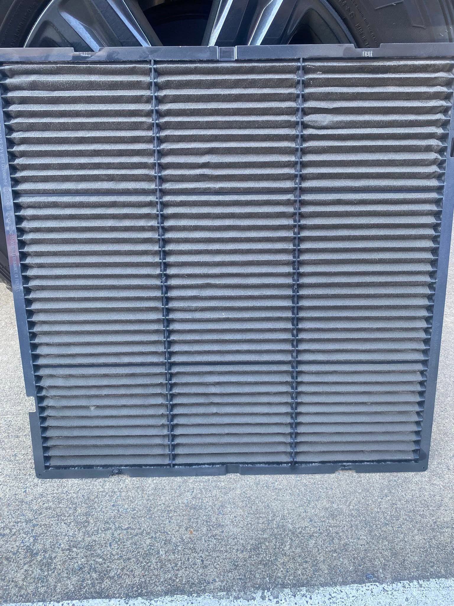 Gray metal slatted vent or grille leaning against a wall on pavement.