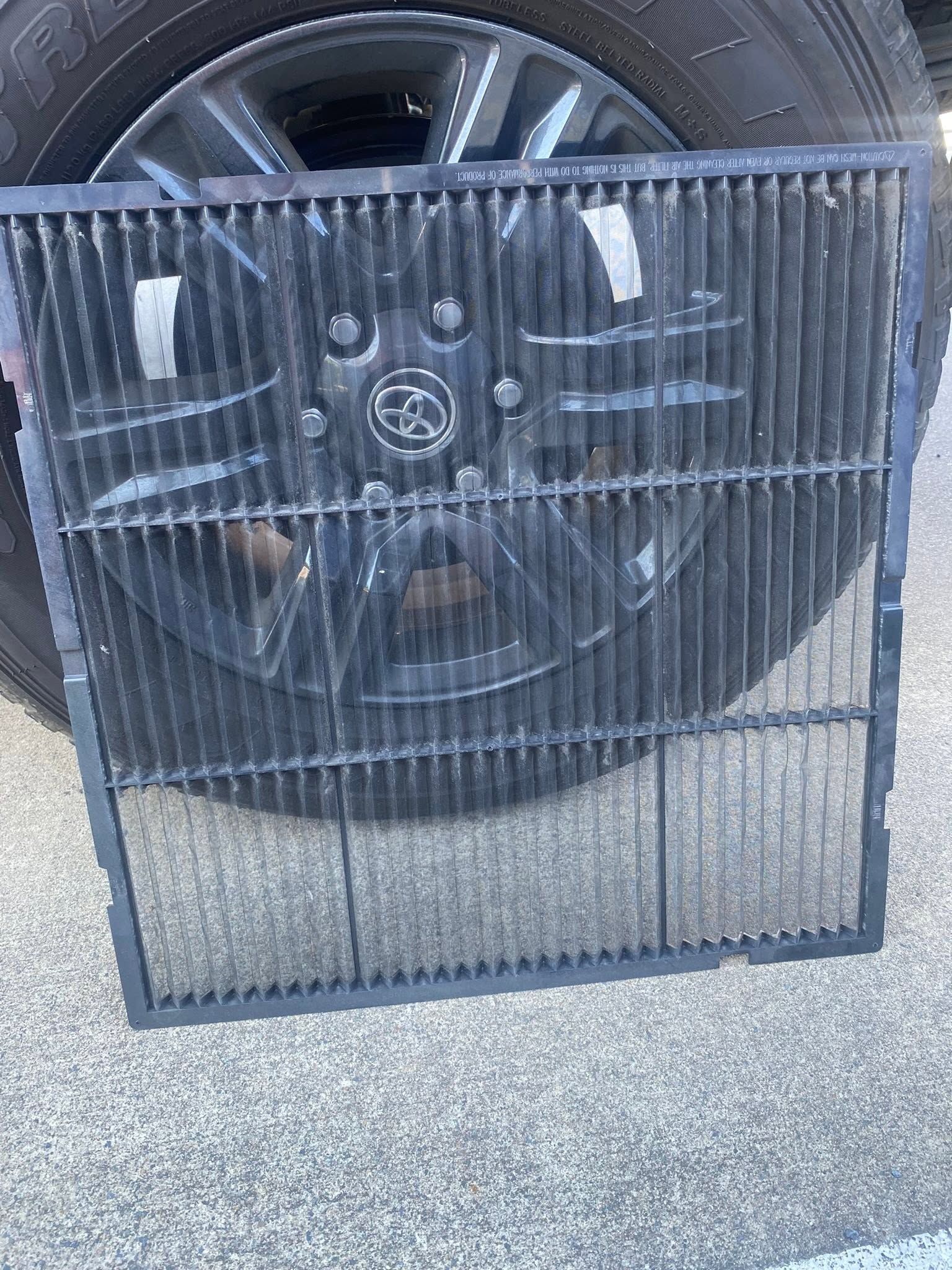 Black metal grille leaning against a car wheel on pavement
