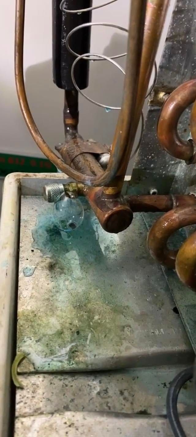 Close-up of a rusty metal pipe and green-stained base with a small valve and coiled tubing.