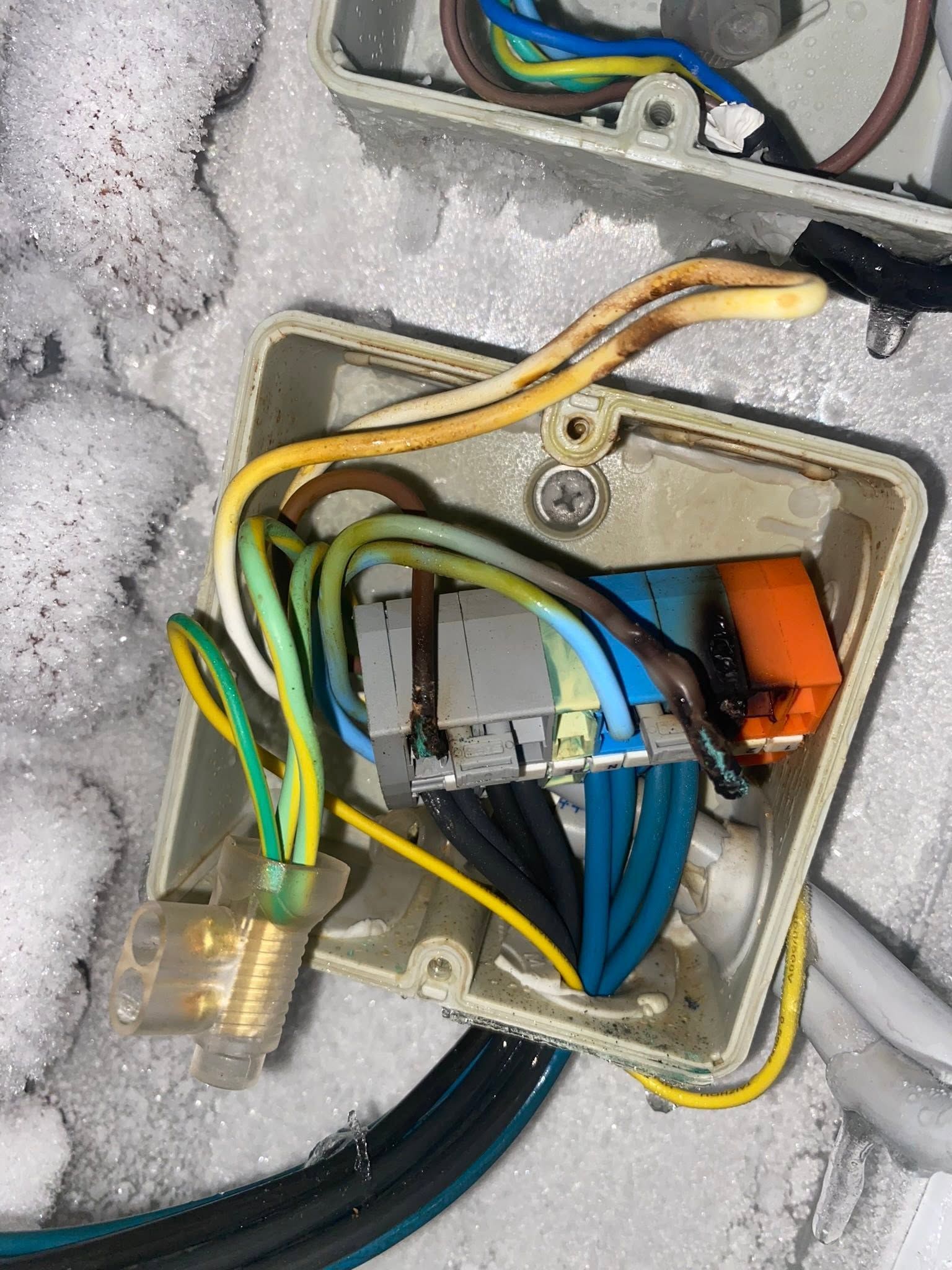 Open electrical junction box with colored wires in snow and ice outdoors
