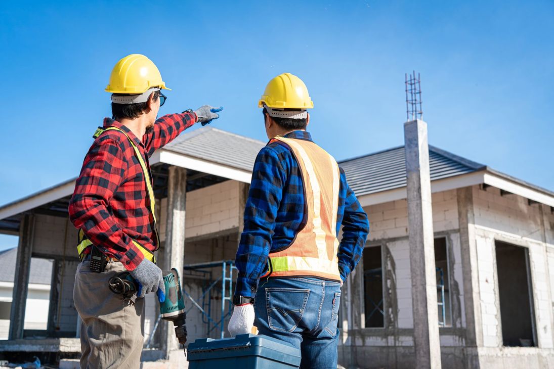 Two construction workers in hard hats inspecting a partially built house.