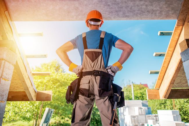 Construction worker in orange hard hat standing on a roof, hands on hips, overlooking the site