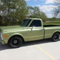 Light green vintage pickup truck parked on a road near trees under a blue sky
