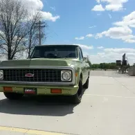 Green GMC pickup parked on a sunny street with trees and blue sky in the background