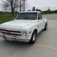 White classic pickup truck parked on a concrete lot with trees and grass in the background
