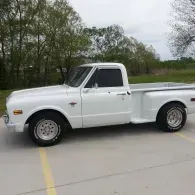 White vintage pickup truck parked on a paved road beside green trees