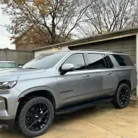 Gray SUV parked in a driveway with black rims and tinted windows, trees and a garage in the background