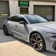 Silver sports sedan parked outside a tint shop with black wheels and tinted windows