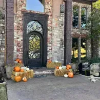 Brick house entrance decorated with pumpkins and fall wreaths at the door