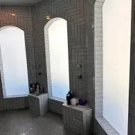 Gray tiled interior with tall arched windows and two small benches beneath them, holding bags and items.
