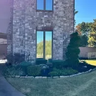 Brick house exterior with tall windows, shrubs, and a curved stone border in a sunny yard