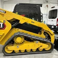 Yellow Caterpillar compact track loader in a workshop, shown side view with black rubber tracks.