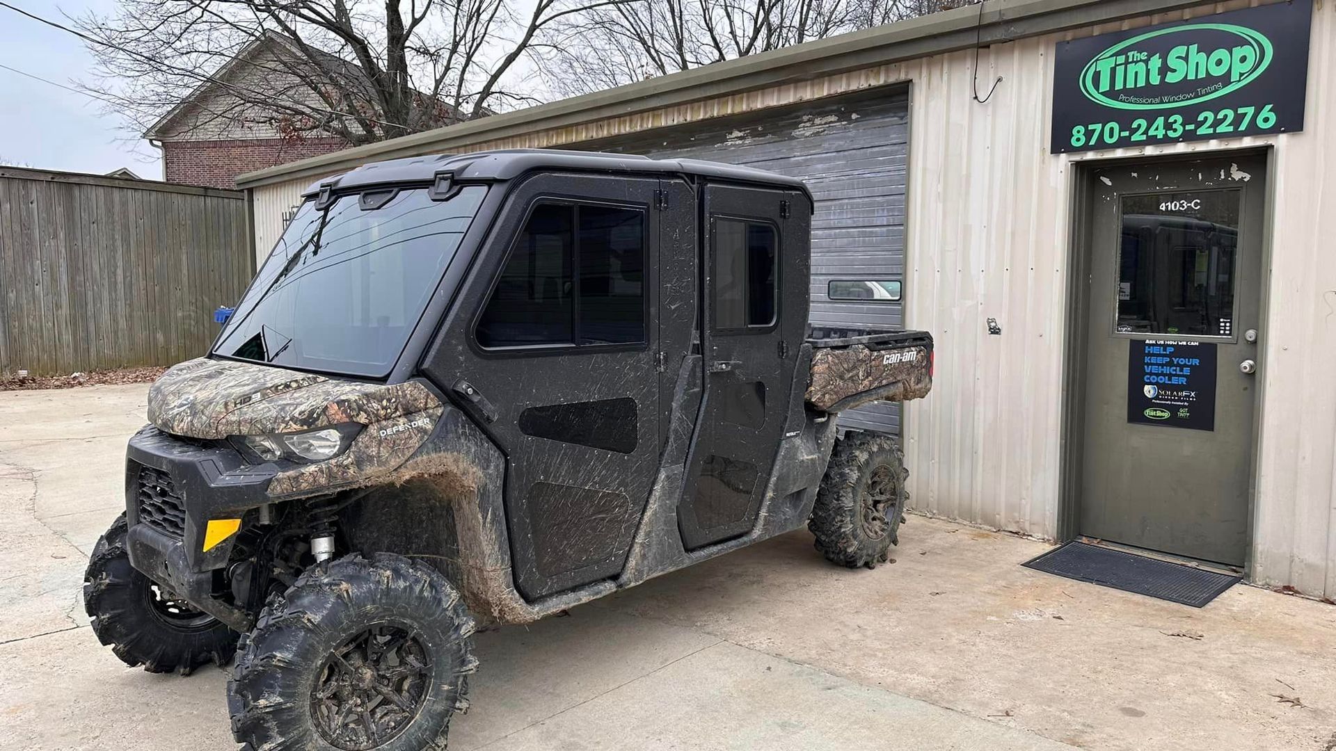 Mud-covered black ATV parked beside a metal shop building with a green sign.