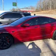 Red sedan parked outdoors beside a black car on a sunny day.