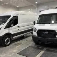 Two white cargo vans parked side by side in a garage or workshop.