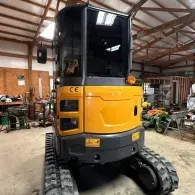 Yellow tracked excavator in a workshop, front view with black cab and rubber tracks