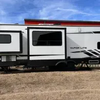 White travel trailer parked in a grassy field under a blue sky