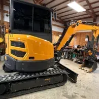 Yellow mini excavator parked inside a workshop garage with another excavator in the background
