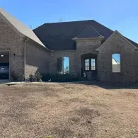 Brick suburban house with a front lawn and arched entryway under a blue sky