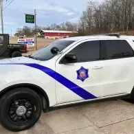 White police SUV with blue stripe and sheriff-style badge parked outside a storefront