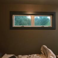 Dim bedroom with a small rectangular window showing trees outside and rumpled bedding in the foreground
