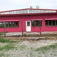 Pink building with a white door, large windows, and a gravel lot in front