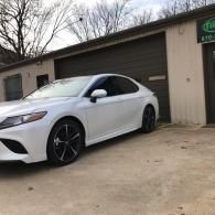 White sedan parked in front of a garage with a brown door on a cloudy day