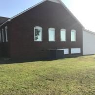 Dark brick house with arched windows and a white garage beside a grassy lawn