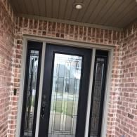 Brick front entry with a black metal security door and covered porch ceiling