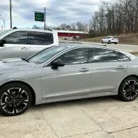 Silver sedan parked on a driveway beside a road, with another white car and trees in the background