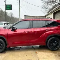 Red SUV parked on a wet driveway beside a house, with black wheels and tinted windows.