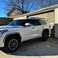 White SUV parked in a driveway beside a garage on a sunny day