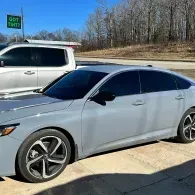 Silver sedan parked beside a white SUV on a sunny roadside, with trees in the background.